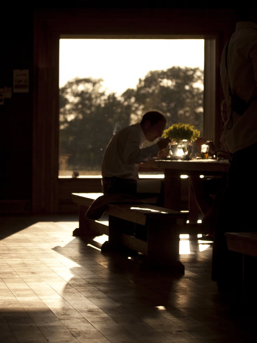 The Gillyflower interior at golden hour, guest dining at bench table with sunset light through large window